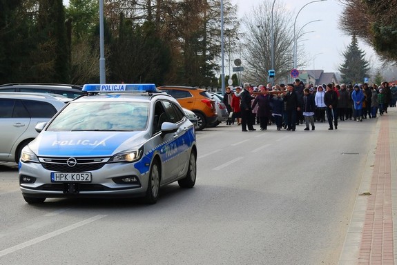 Policyjny radiowóz na przedzie kolumny pielgrzymów w czasie drogi krzyżowej ulicami miasta. W tle uczestnicy procesji