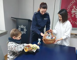 Policjantka częstuje się słodyczami, które zostały przyniesione przez dzieci. Obok siedzi mały chłopiec, który je cukierka.