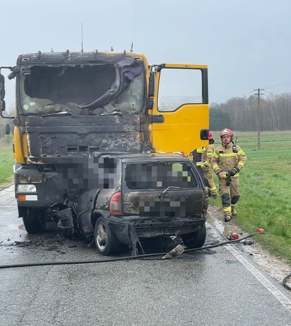 Na drodze stoją osobówka , która uderzyła w ciężarówka. Opel jest całkowicie spalony, a cięzarówka ma spalony przód.