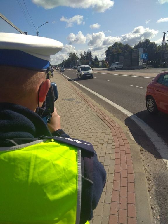 Funkcjonariusz sprawdzający prędkość z jaka poruszają się pojazdy. w tle samochody jadące ulicą