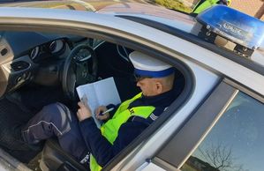 Policjant ruchu drogowego siedzący w radiowozie, sprawdzający dokumenty podczas kontroli drogowej