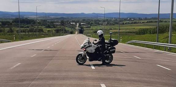 Zdjęcie przedstawia umundurowanego policjanta na motocyklu służbowym. motocykl soi na drodze.
