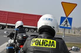Na zdjęciu dwaj umundurowani policjanci ruchu drogowego na motocyklach. W tle pojazd ciężarowy z naczepą