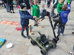 Na zdjęciu dzieci przy robocie pirotechnicznym. Robot obiera od jednego z dzieci element z drewna.