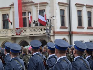 zdjęcie wykonane od tyłu, na pierwszym planie policjanci kompanii honorowej, zwróceni w kierunku masztu i flagi, które są rozmyte na drugim planie
