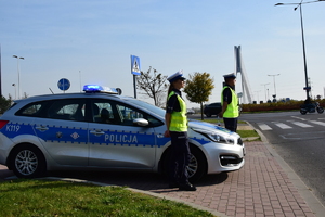 Dwoje policjantów stojących przy radiowozie, w tle ulica, pora dzienna