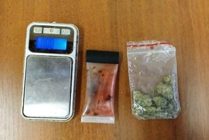 Waga gramowa obok której znajduje się tester narkotykowy oraz woreczek strunowy  z zawartością suszu roślinnego.