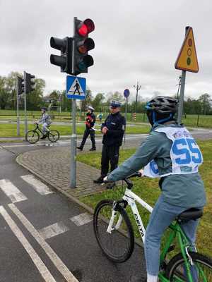 Na zdjęciu osoby biorące udział w turnieju ruchu drogowego. Rowerzysta stojący przez sygnalizatorem świetlnym emitującym światło czerwone