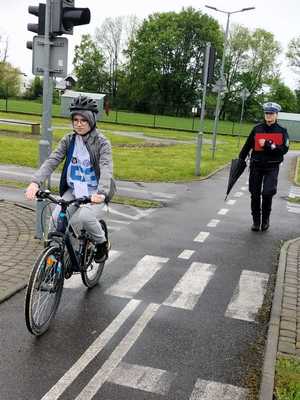 Na zdjęciu osoby biorące udział w turnieju ruchu drogowego. Rowerzysta jadący jednośladem, z tyłu za nim umundurowana policjantka