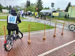 Na zdjęciu osoby biorące udział w turnieju ruchu drogowego. Rowerzysta jadący slalomem pomiędzy przeszkodami.