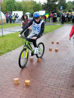 Na zdjęciu osoby biorące udział w turnieju ruchu drogowego. Rowerzysta przejeżdżający przez przeszkody ustawione na drodze
