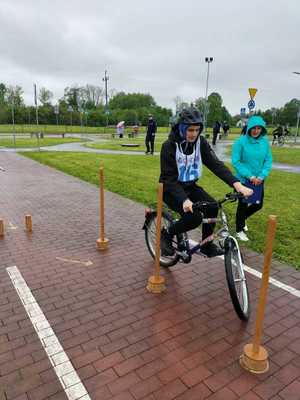 Na zdjęciu osoby biorące udział w turnieju ruchu drogowego. Rowerzysta  omijający przeszkody ustawione na drodze.