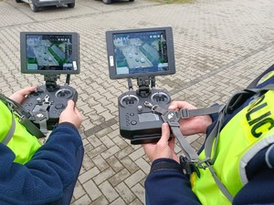Zdjęcie przedstawia funkcjonariuszy Policji którzy w rękach trzymają urządzenie do sterowania dronem policyjnym .