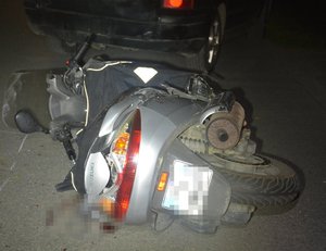 Uszkodzony motocykl leżący na jezdni, w tle pojazd sprawcy zdarzenia