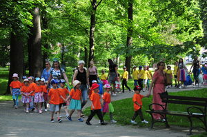Duża ilość dzieci poubierana w pomarańczowe i żółte koszulki idą na spotkanie wraz z przedszkolankami