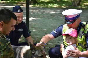 Policjanci, funkcjonariusz Straży Granicznej i dziecko. Obok dziecka pies służbowy
