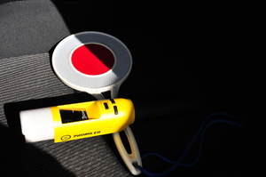 Leżąca na siedzeniu radiowozu tarcza do zatrzymywania pojazdów oraz policyjny alkomat koloru żółtego