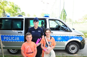 Policjantka oraz dwie dziewczynki pozujące do zdjęcia przed radiowozem