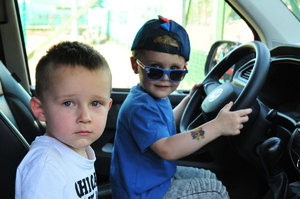 Dwóch chłopców wewnątrz radiowozu. Jeden z nich siedzi za jego kierownicą