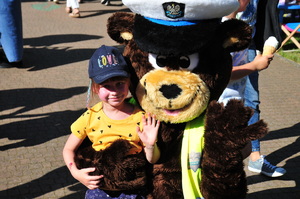 Maskotka jasielskiej policji przytulająca dziewczynkę i machająca