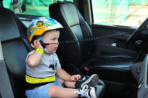Mały chłopiec siedzący wewnątrz radiowozu i przykładający do ucha mikrofon do stacji radiowej