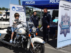 umundurowani policjanci przy policyjnym stoisku, na pierwszym planie chłopiec siedzący na policyjnym motocyklu