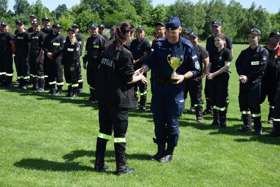Policjant odbiera Puchar od funkcjonariuszki strazy pozarnej