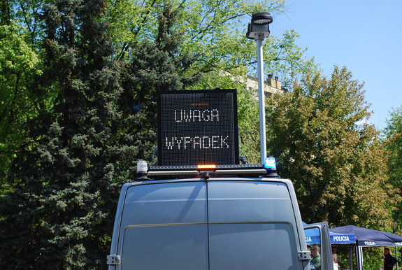 Na zdjęciu policyjny ambulans z rozłożoną tablica informująca o wypadku. Na tablicy świetlnej napis uwaga wypadek.