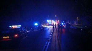 Zdjęcie wykonane nocą. Na ulicy stoją pojazdy policji i straży pożarnej z łączonymi światłami błyskowymi.