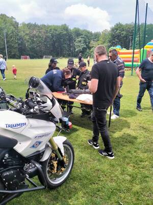 z tyłu widoczna policjantka wykonująca odciski palców , obok stojące inne osoby