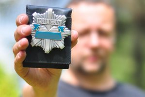 Na pierwszym planie policyjna odznaka, na drugim planie rozmazana postać, która trzyma odznakę.