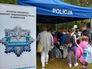 na zdjęciu widoczny namiot z napisem Policja, pod którym znajdują się ludzie, z lewej strony roll up z napisem Wydział Prewencji, Komenda Wojewódzka Policji w Rzeszowie