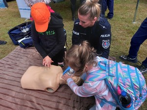 dziecko ćwiczące resuscytację na manekinie, obok policjantka