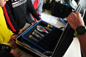 Wnętrze walizki zawierające narzędzia wykorzystywane przez technika kryminalistyki. Wokół widać zebrane dzieci.