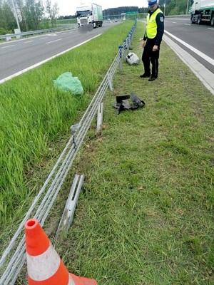 policjant stoi przy barierach energochłonnych dzielących pasy jezdni na drodze szybkiego ruchu