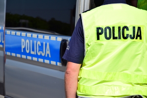policjant w żółtej kamizelce z napisem policja na plecach, w tle radiowóz