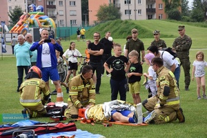 Strażacy podczas pokazu ratownictwa, pomagający mężczyźnie leżącemu na desce. W tle widzowie