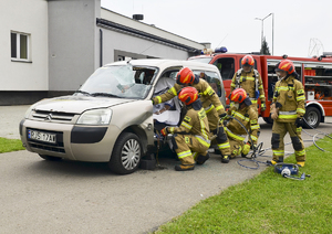 Strażacy podczas pokazu ratownictwa wycinający i wyciągający pozoranta z samochodu