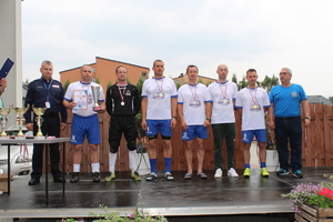Zawodnicy PSP z pucharem, dyplomem oraz medalami na szyi oraz organizator, komendanci jasielskiej policji i straży pożarnej pozujący do zdjęcia na scenie podczas ceremonii wręczania nagród.