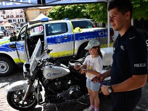 umundurowany policjant przy motocyklu oraz dziewczynka zakładająca na rękę opaskę odblaskową