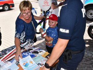 kobieta z dzieckiem przy stoisku policyjnym zabiera ze stolika materiały profilaktyczne, ulotki i broszury