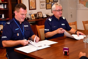 Komendant Wojewódzki Policji w Rzeszowie podpisuje porozumienie w gabinecie przy stole. Na zdjęciu Komendant Wojewódzki Policji i zaproszeni goście w trakcie podpisywania porozumienia