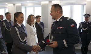 Zdjęcie przedstawia wnętrze sali, w której ustawieni są pracownicy Policji, umundurowani policjanci, poczet sztandarowy. Policjanci i pracownicy odbierają odznaczenia od Komendanta.