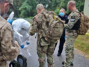 policjantka zabezpiecza ślady kryminalistyczne, wokół niej umundurowani przedstawiciele innych służb