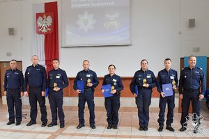 umundurowani policjanci ustawieni w szeregu na scenie z nagrodami i pucharami