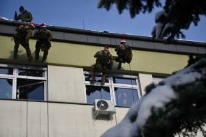 Policyjni kontrterroryśći zjeżdżają na linach z dachu i wręczają dzieciom w szpitalu prezenty.