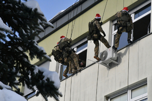 Policyjni kontrterroryśći zjeżdżają na linach z dachu i wręczają dzieciom w szpitalu prezenty.