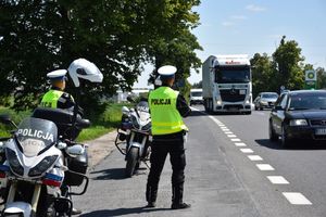 na zdjęciu umundurowani policjanci, w żółtych kamizelkach, stojący na drodze wykonujący pomiary prędkości