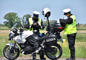 na zdjęciu umundurowani policjanci, w żółtych kamizelkach, stojący na drodze wykonujący pomiary prędkości