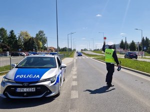 na zdjęciu umundurowani policjanci, w żółtych kamizelkach, stojący na drodze wykonujący pomiary prędkości